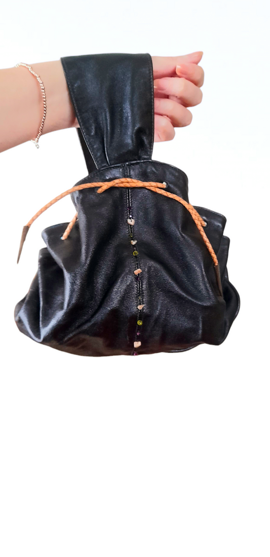 Black faux leather drawstring pouch wristlet bag by London designer Sara Efia Reddin. Shown hanging on an arm.
